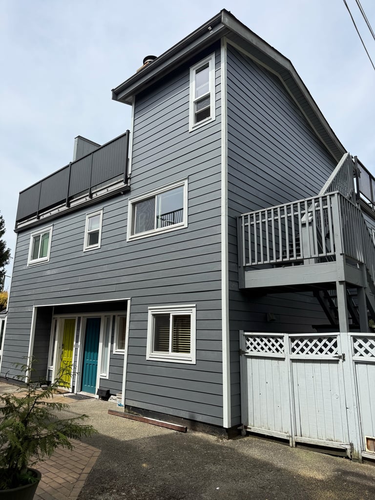 Modern gray and white multi-story house with elevated deck, white railings, and garage on brick driveway